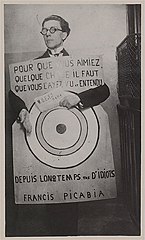 André Breton avec une affiche créée par Francis Picabia, “Pour que vous aimiez quelque chose il faut que vous l'ayez vu et entendu depuis longtemps tas d'idiots”, 1920